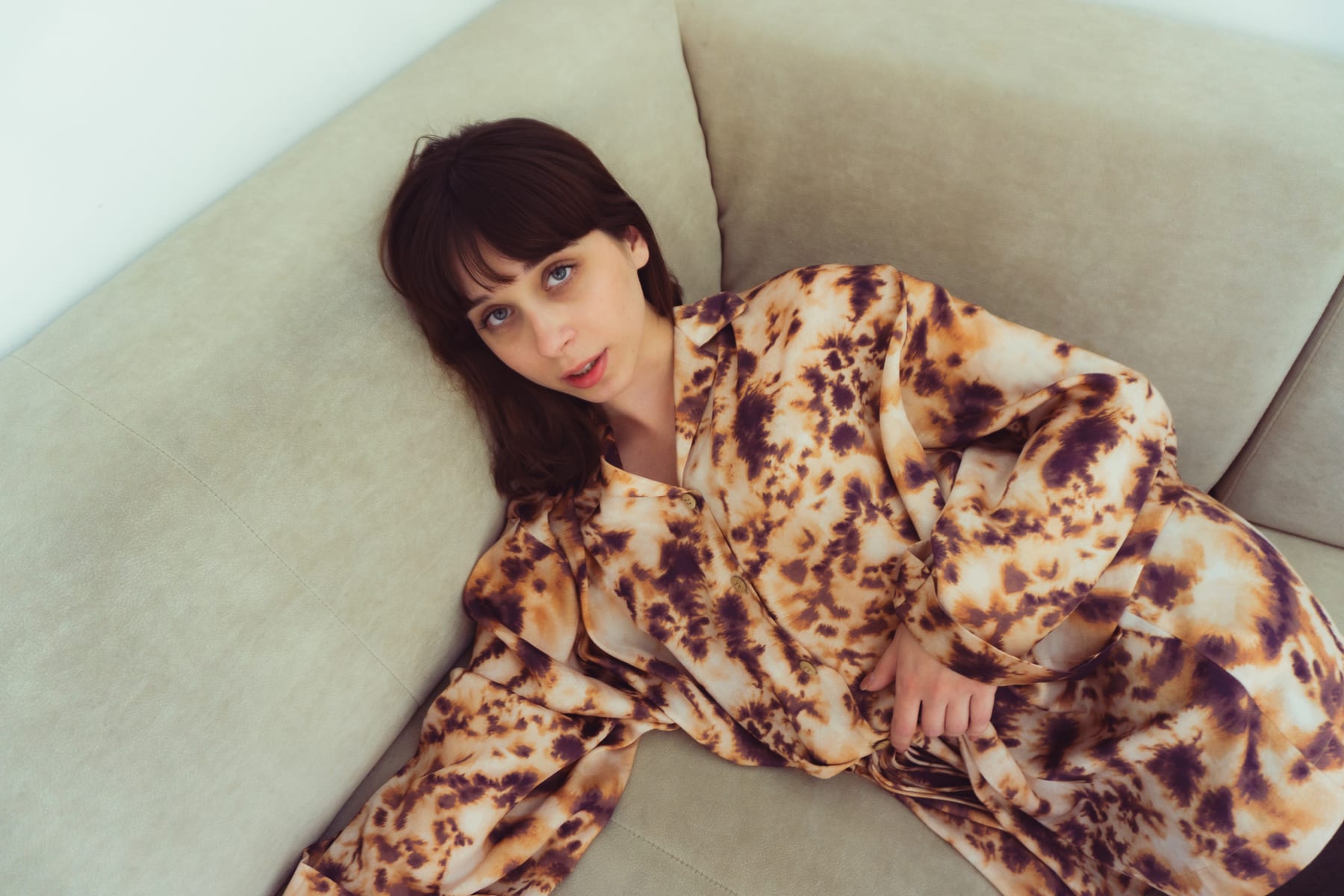 Bogi in an animal-print silk pyjama set lying in the corner of a beige sofa.