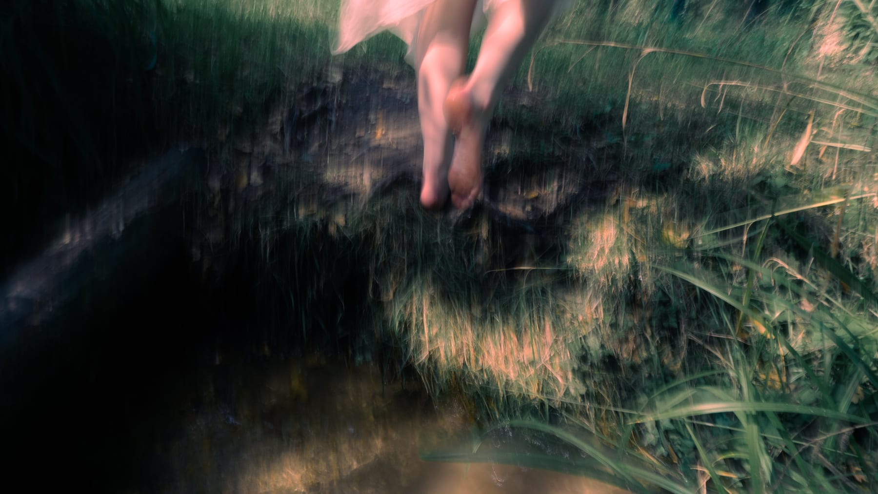 Motion-blurred bare feet stepping through long grass.