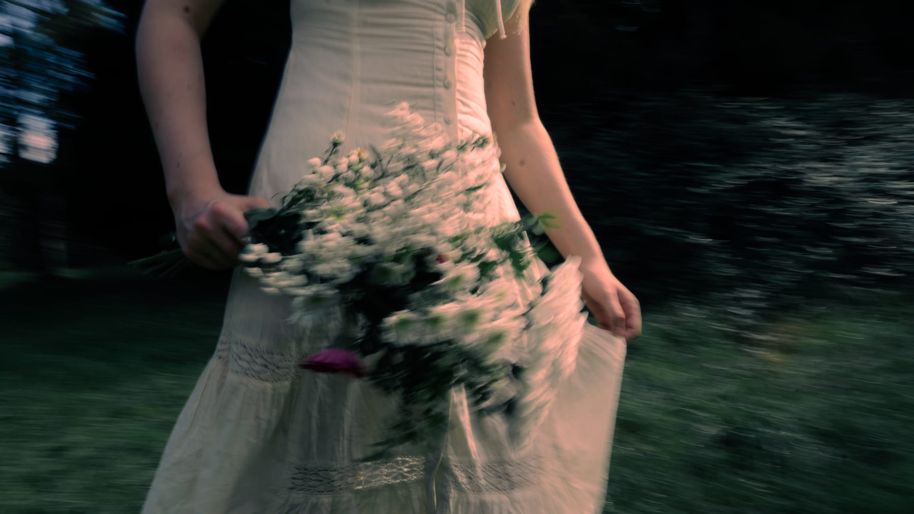 A pale dress and a bunch of white wild flowers in motion, close up.