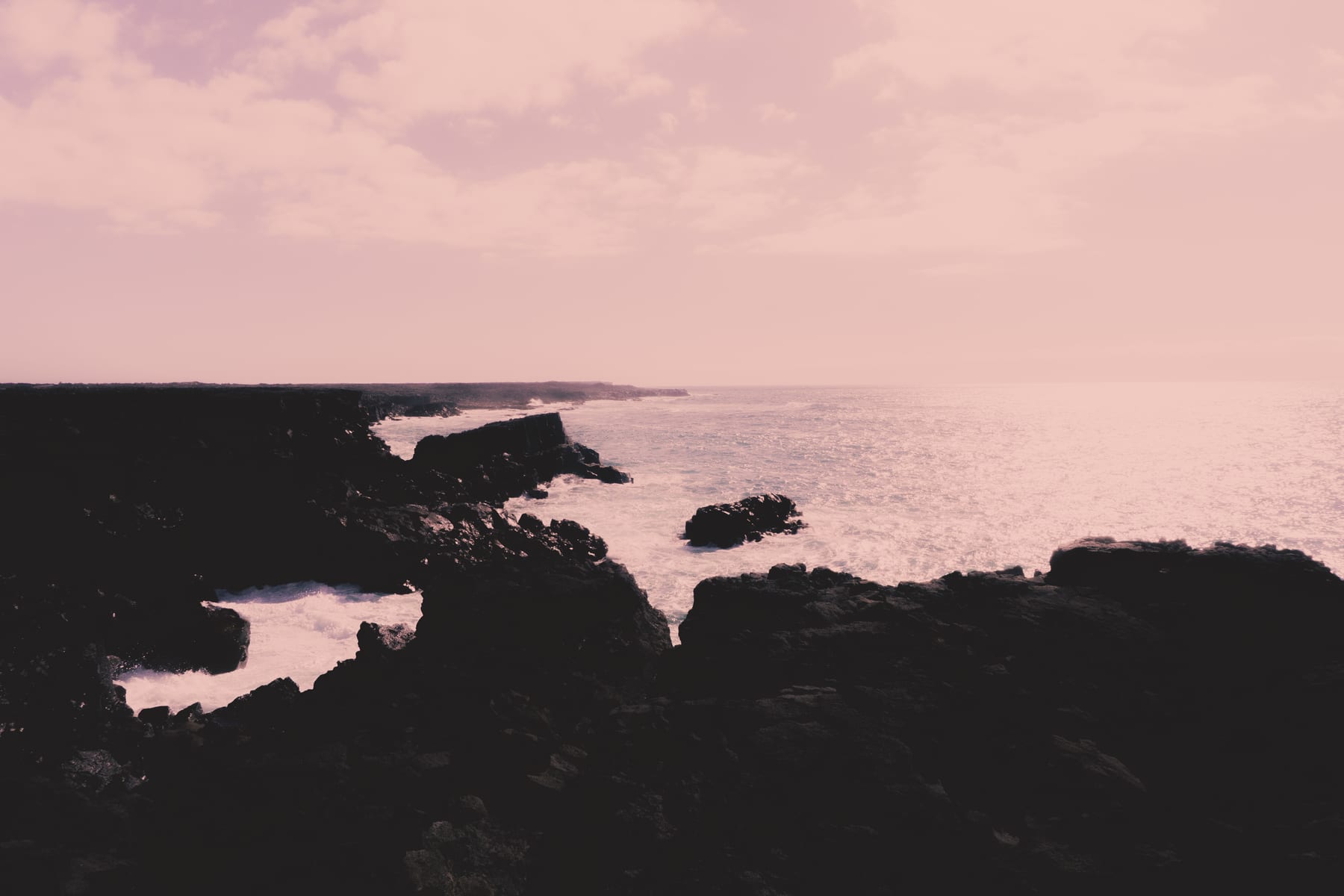 A dark rocky shore in Iceland with waves breaking white on the stones.