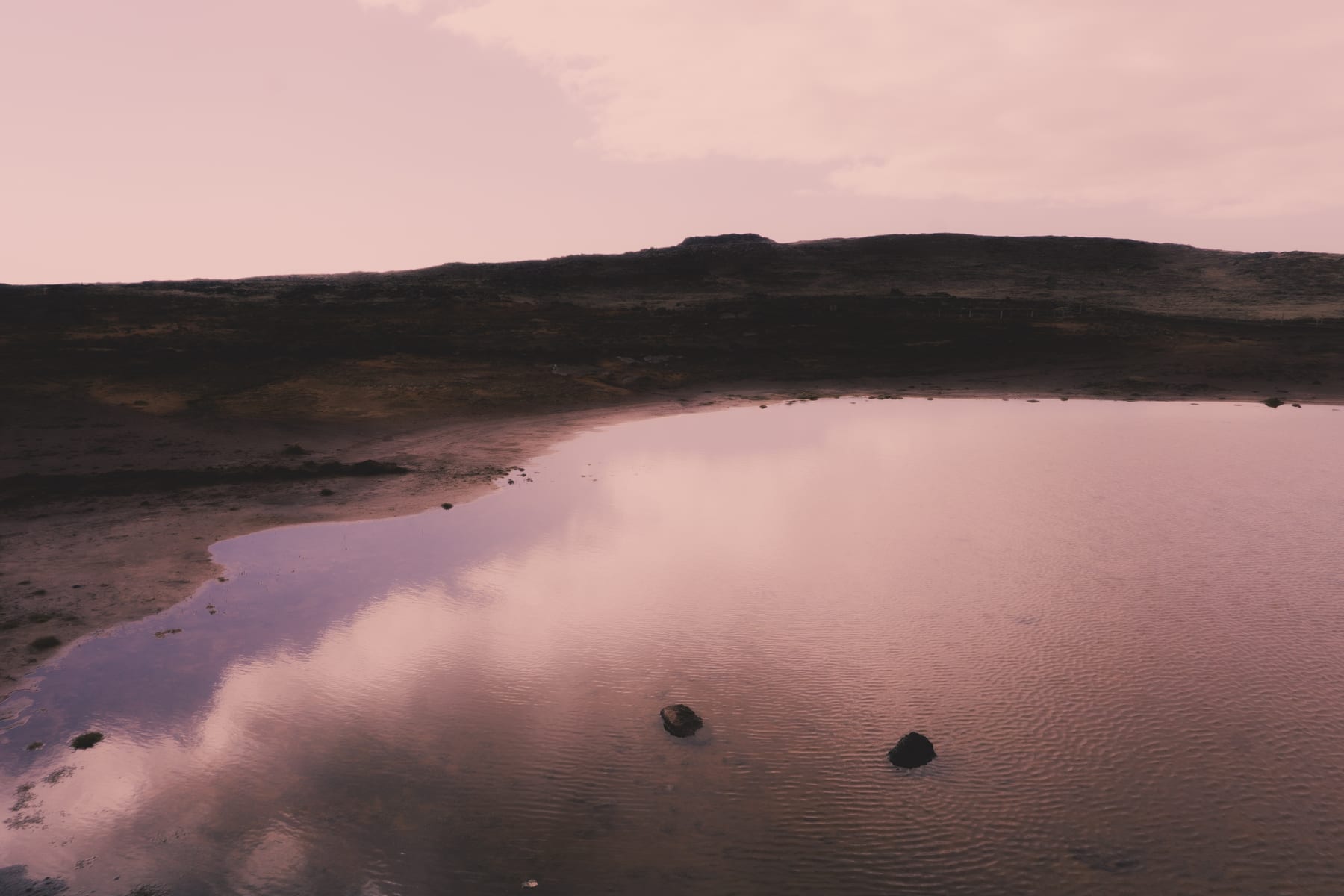 A shallow lake mirroring the cloudy sky below a low hill, Iceland.