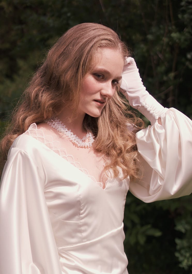 Magnolia Girls for Fanni Sutus: model with long wavy hair in a white satin blouse, raising a sleeve to her face.