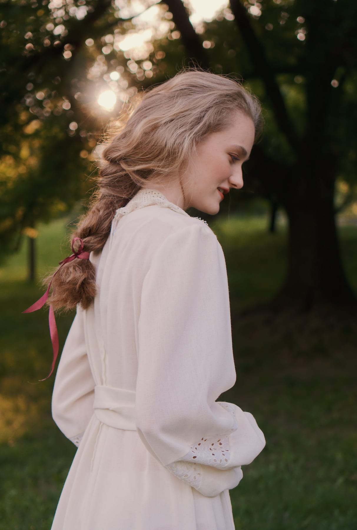 Model in a white dress with a long braid among trees in evening light, Magnolia Girls behind the scenes.