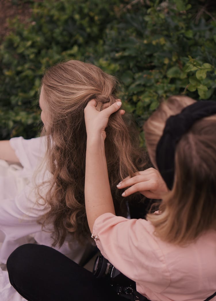 A stylist pinning up a model's long blonde hair outdoors, behind the scenes of Magnolia Girls.