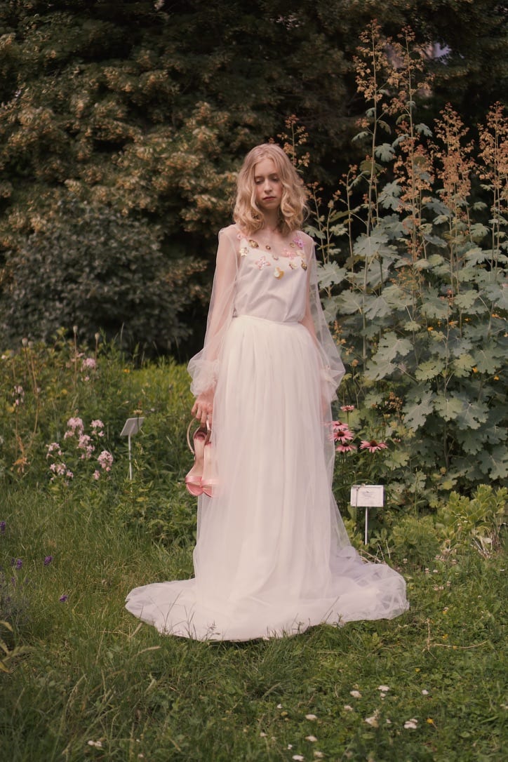 Model in a long white tulle dress standing among flowers in a green garden, Magnolia Girls.