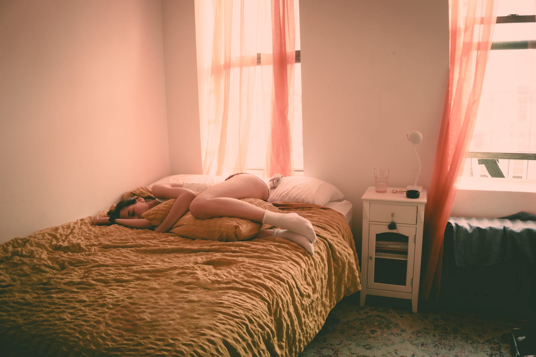 A sunlit bedroom with a gold bedspread and pink curtains in a New York apartment.