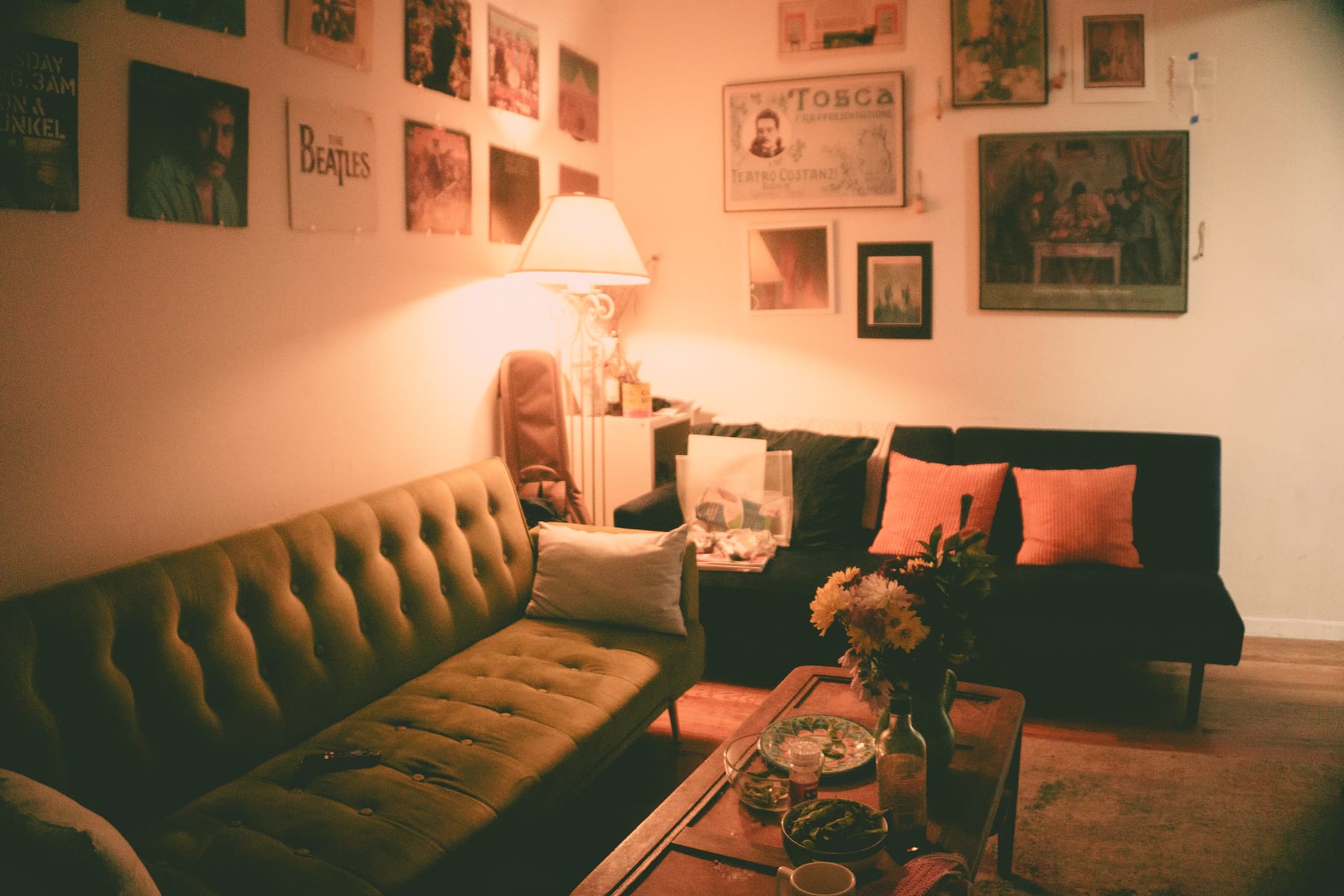 A warmly lit New York living room with a green velvet sofa and framed posters on the walls.