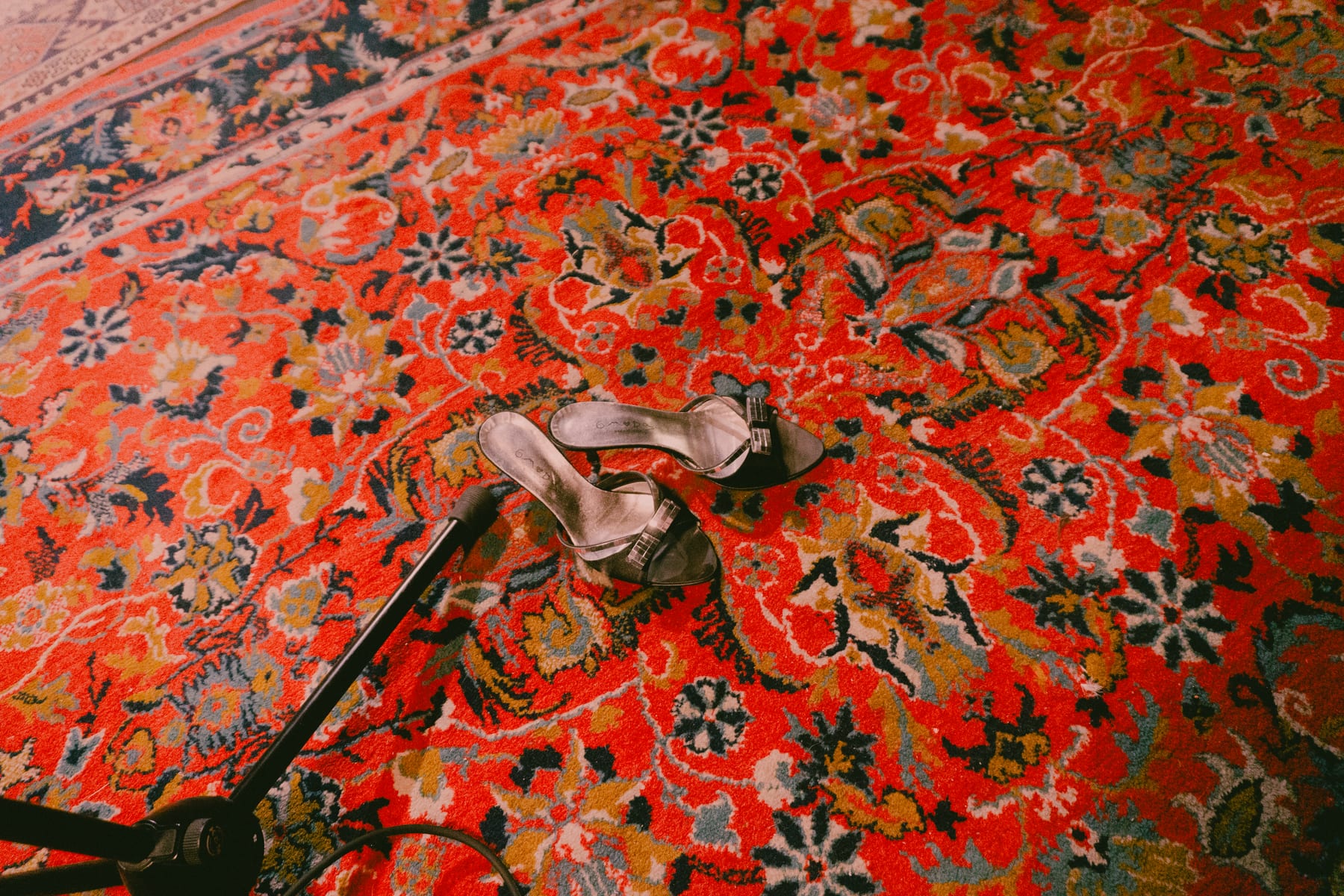 Silver high heels left on a red Persian rug beside a microphone stand.