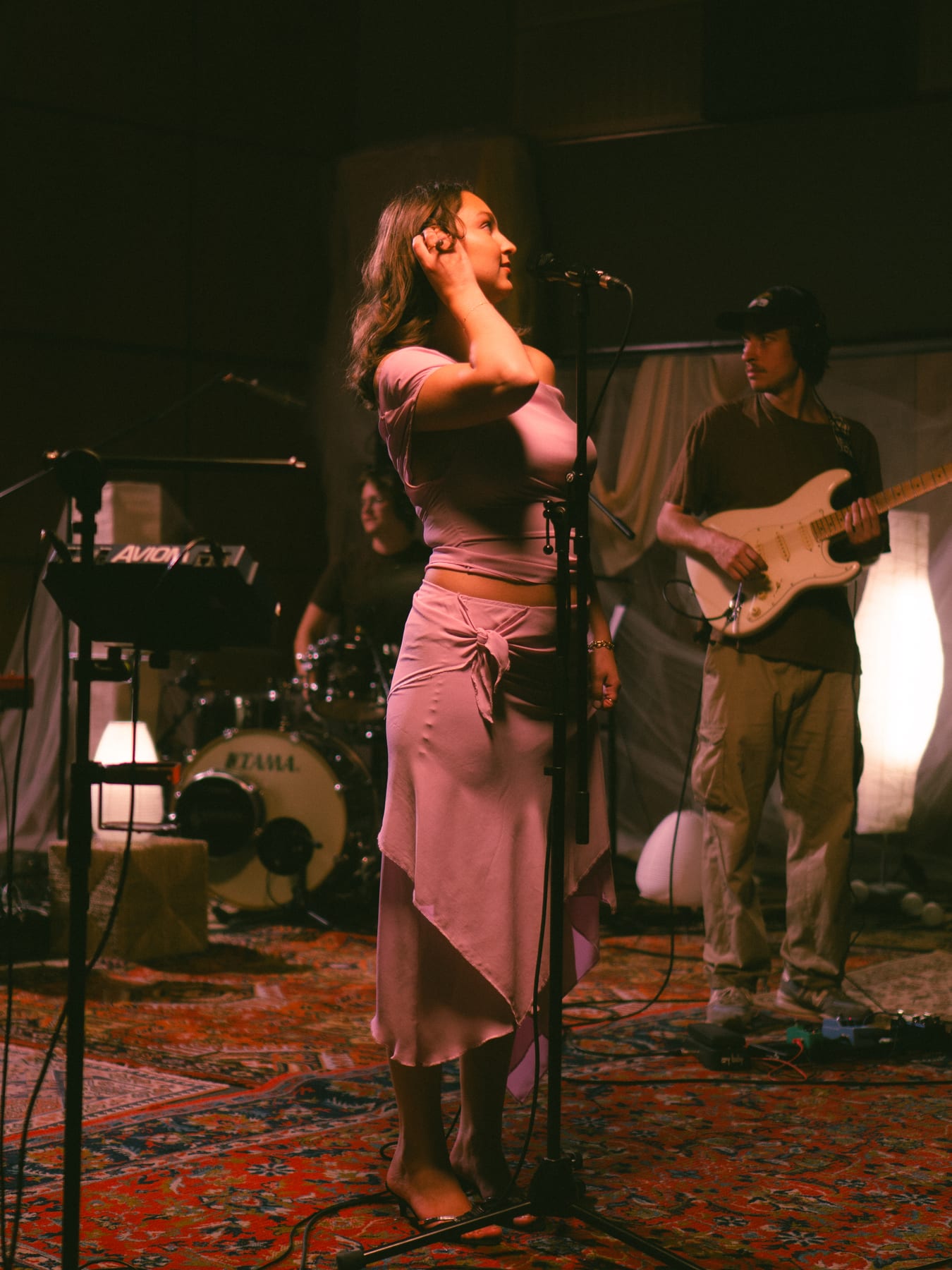 Pati Piko at the microphone in a pink dress beside a guitarist, live session.
